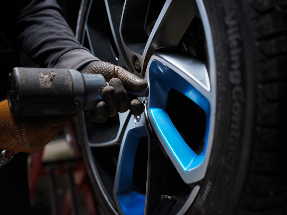 A close-up image of a gloved hand and drill tightening the bolts on a Lynk & Co car wheel. 