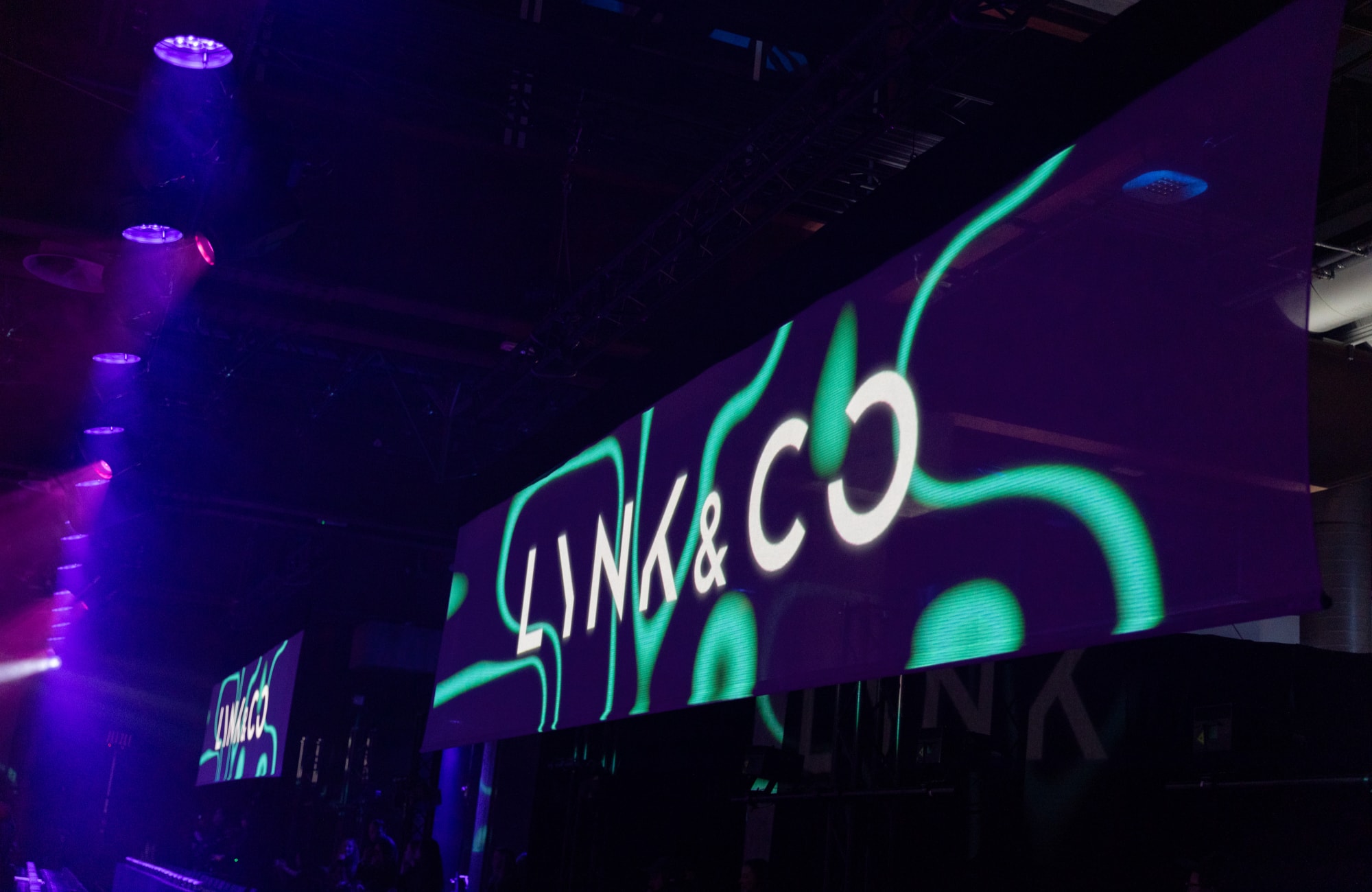 Image of the Lynk & Co logo with a green background pattern, displayed on a large digital screen, viewed from a side angle. 