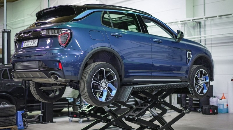 An image of a Lynk & Co car in a a workshop environment. The car is lifted off the ground on a hydraulic platform. 