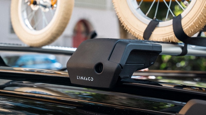 An image of a Lynk & Co roof rack mounted on top of a car. The wheels of a child’s bike are visible, attached to the rack.