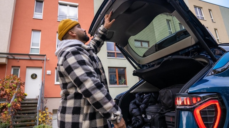An image of a man standing at the rear of a Lynk & Co car and raising his hand to open or close the trunk door. 