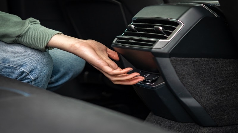A close-up image of a hand pressing a button on a car’s interior. 